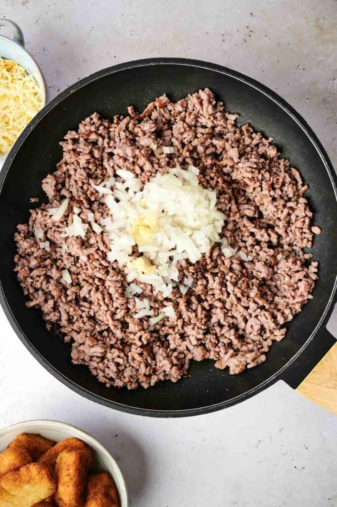Ground beef and onion in a large skillet for a tater tot casserole dish.