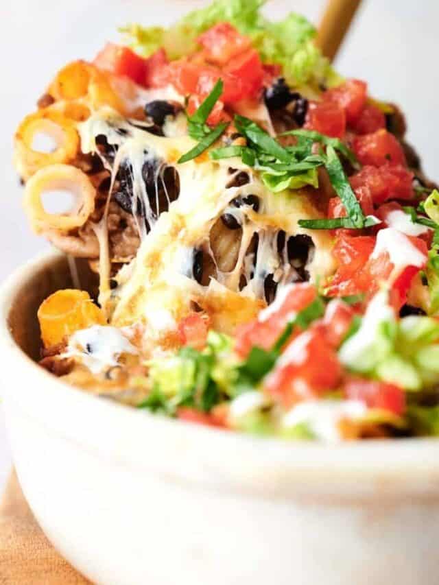 A close-up of a bowl of nachos topped with melted cheese, sour cream, tomatoes, and lettuce.