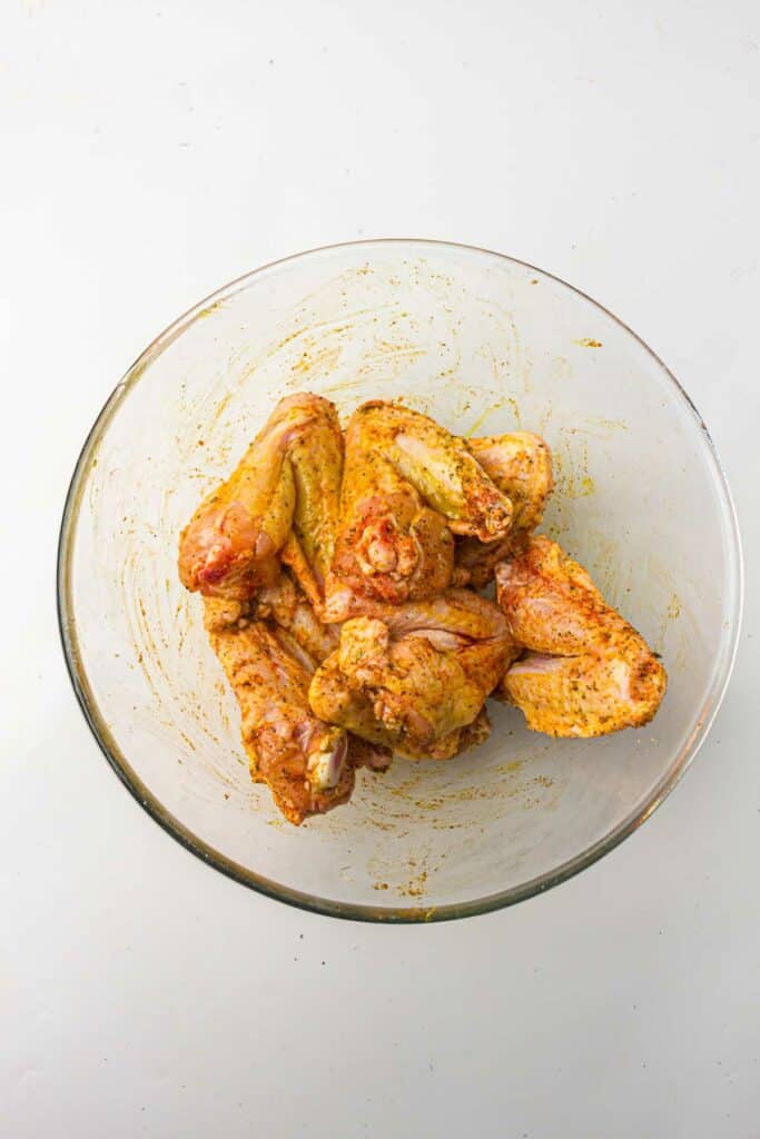Chicken wings in a bowl with seasonings.