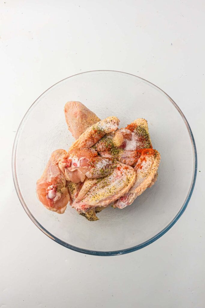 Chicken wings in a bowl with seasonings.