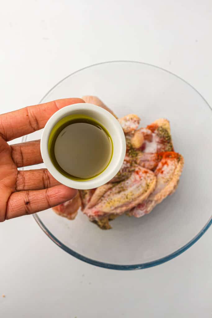 Chicken wings in a bowl with seasonings and a cup of avocado oil. 
