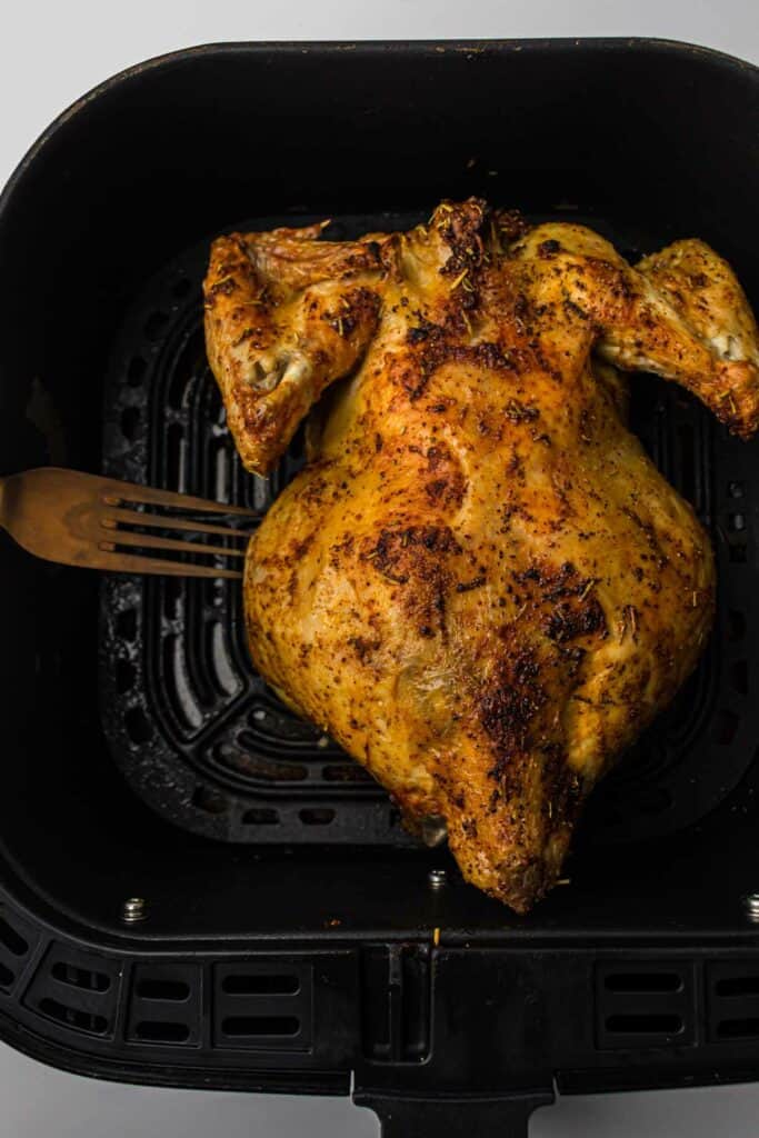 A whole chicken in an air fryer with a fork.