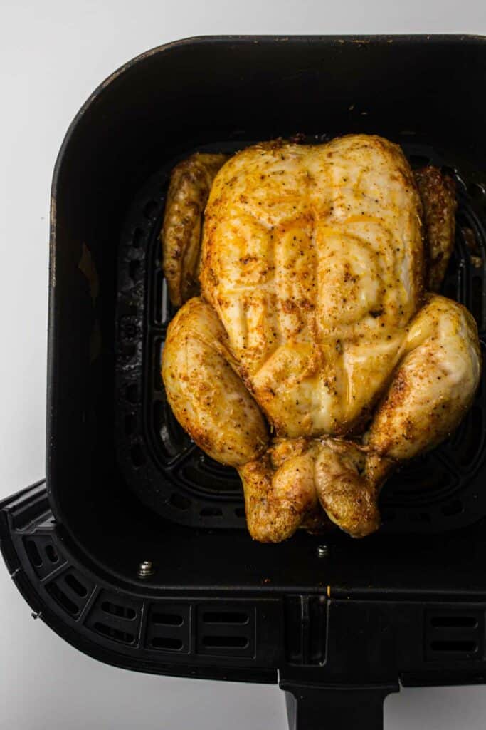 A whole chicken in an air fryer on a white background.