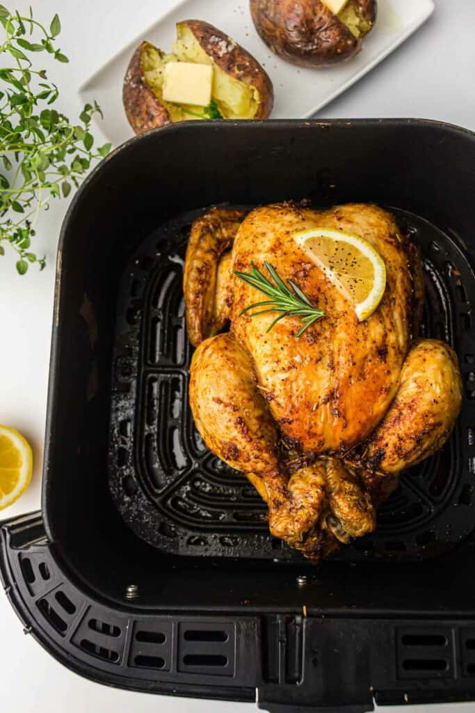 A whole chicken in an air fryer with lemon and potatoes.