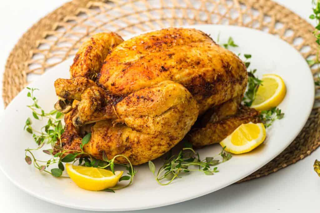 A whole chicken roasted in an air fryer, served on a plate with lemons and herbs.