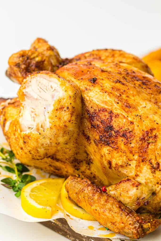 A succulent roasted chicken on a plate with lemon wedges, cooked in an air fryer.