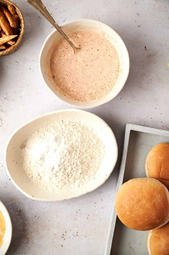 A bowl of flour and seasonings next to a bowl of ketchup.