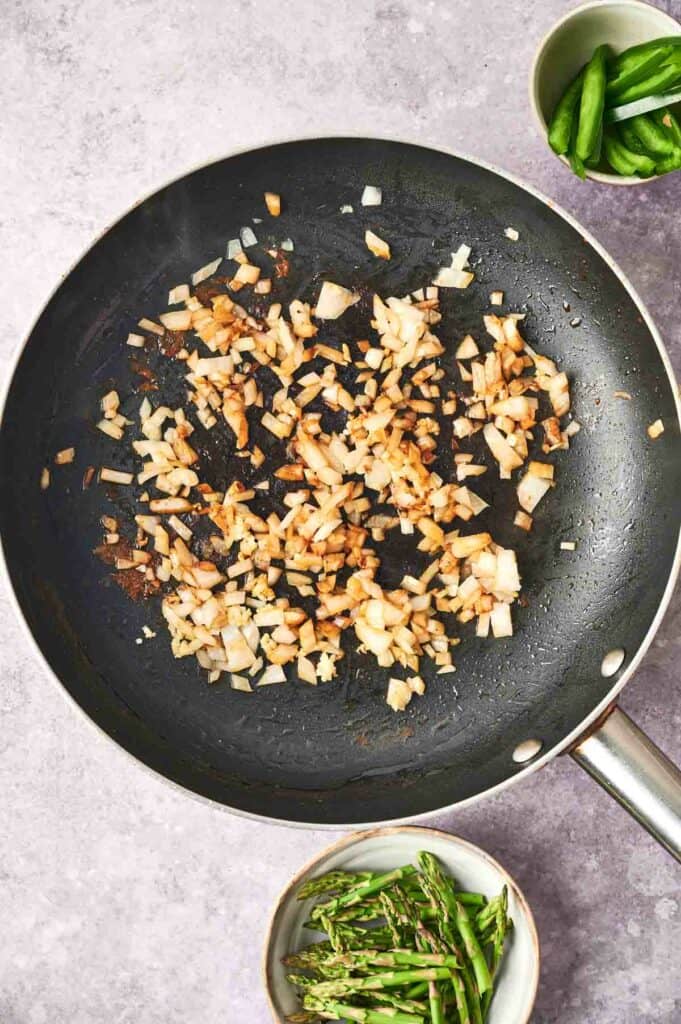 A frying pan with onion and garlic sizzling.