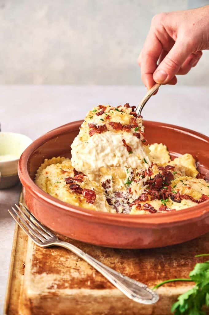 A person holding a fork over a bowl of Olive Garden's Ravioli Carbonara.
