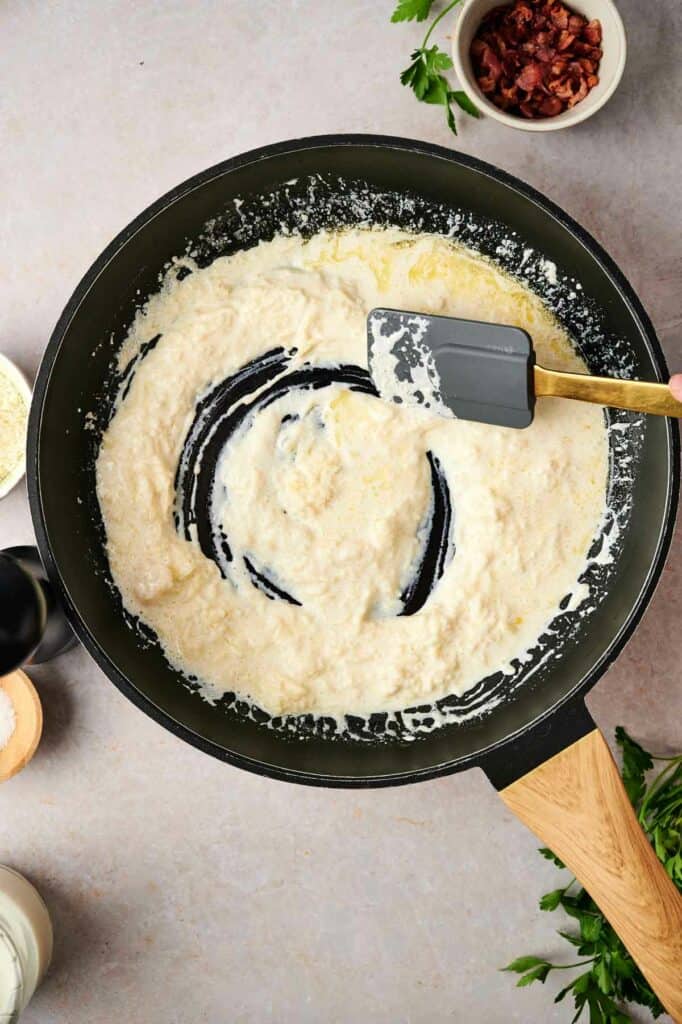 A frying pan with ingredients, including olive garden ravioli carbonara, being stirred with a wooden spoon.