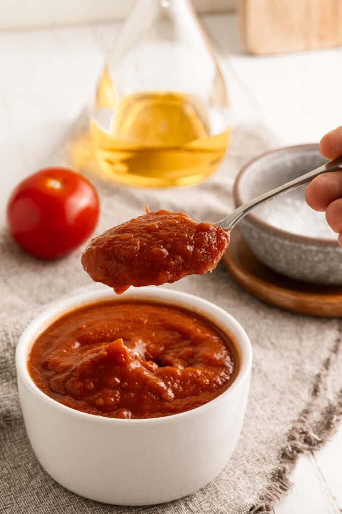 A person is pouring tomato sauce into a bowl.