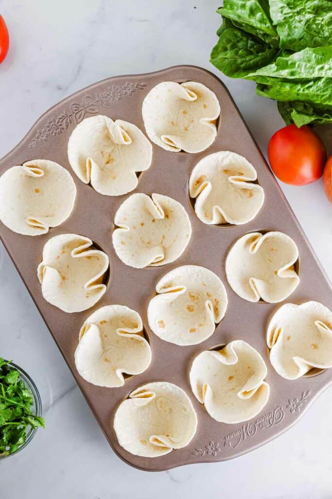A tray full of taco salad cups and vegetables on a marble countertop.