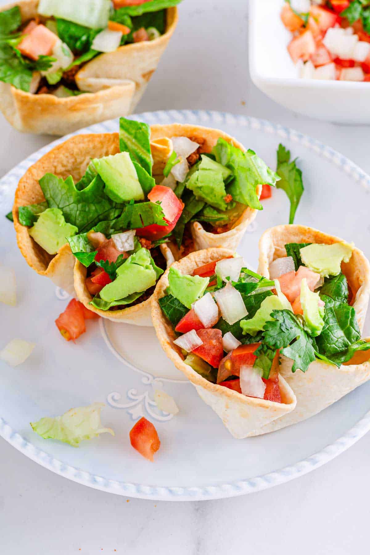 A plate of taco salad cups on a table next to a bowl of salsa.