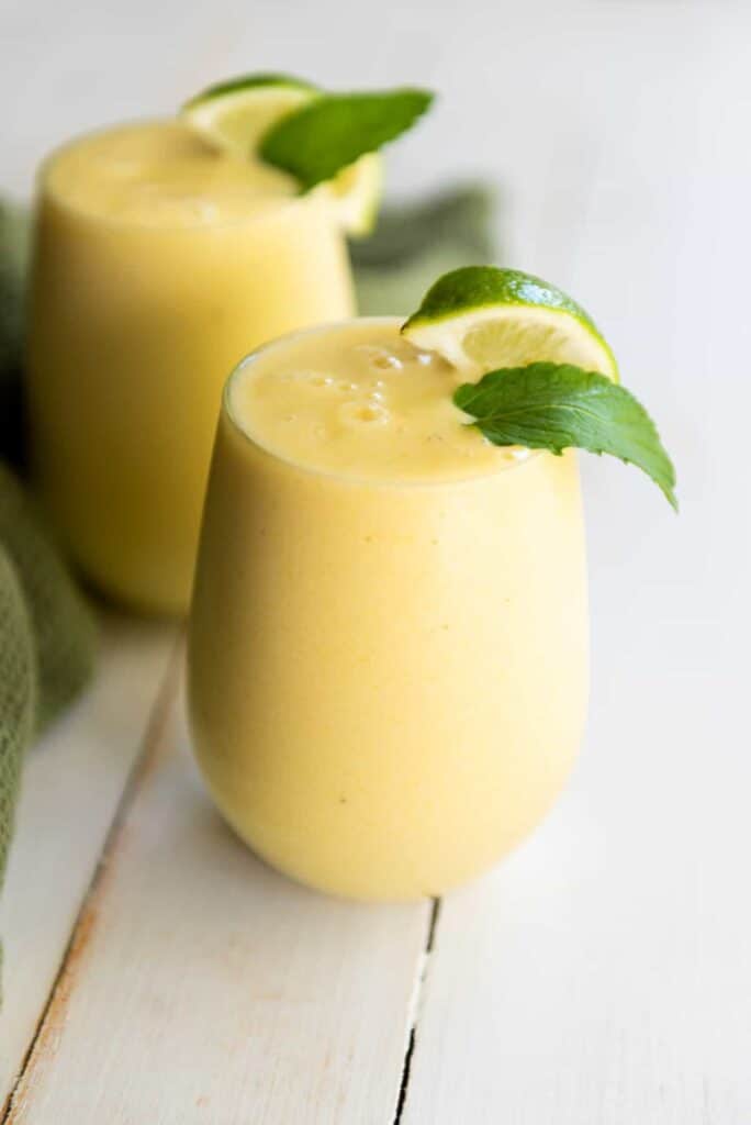 Two glasses of mango smoothie on a wooden table.