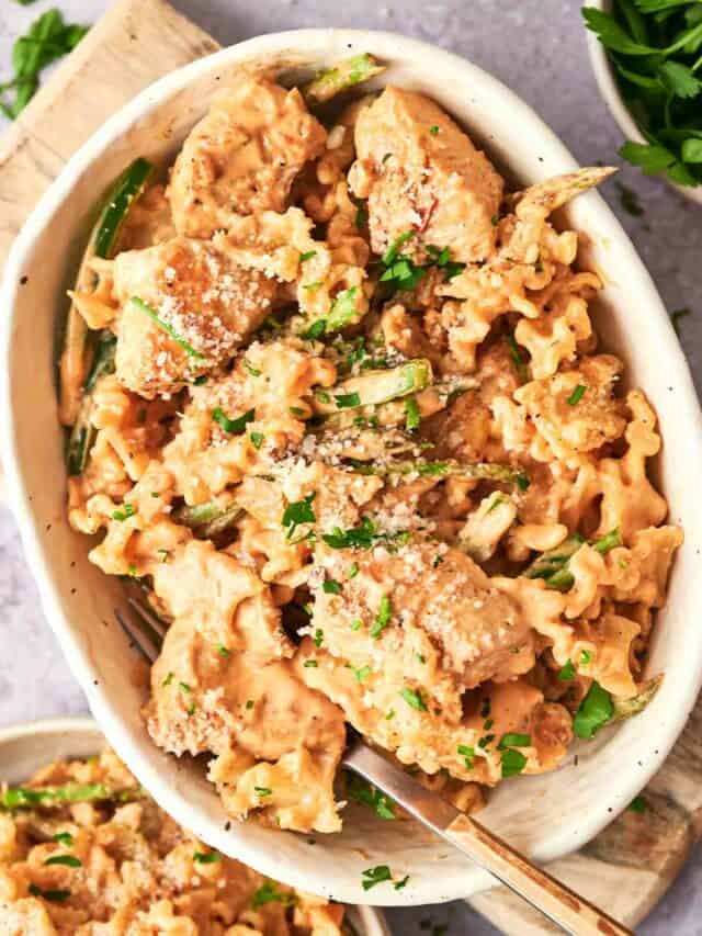 A bowl of creamy pasta with green herbs and a sprinkle of sesame seeds.