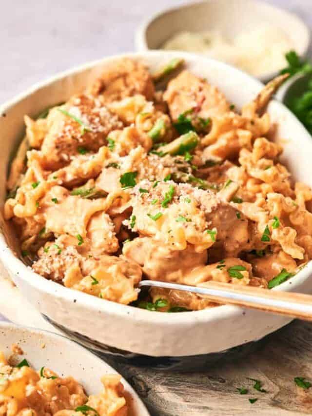 A bowl of pasta with a creamy sauce, garnished with parsley and grated cheese, with a fork in the bowl.