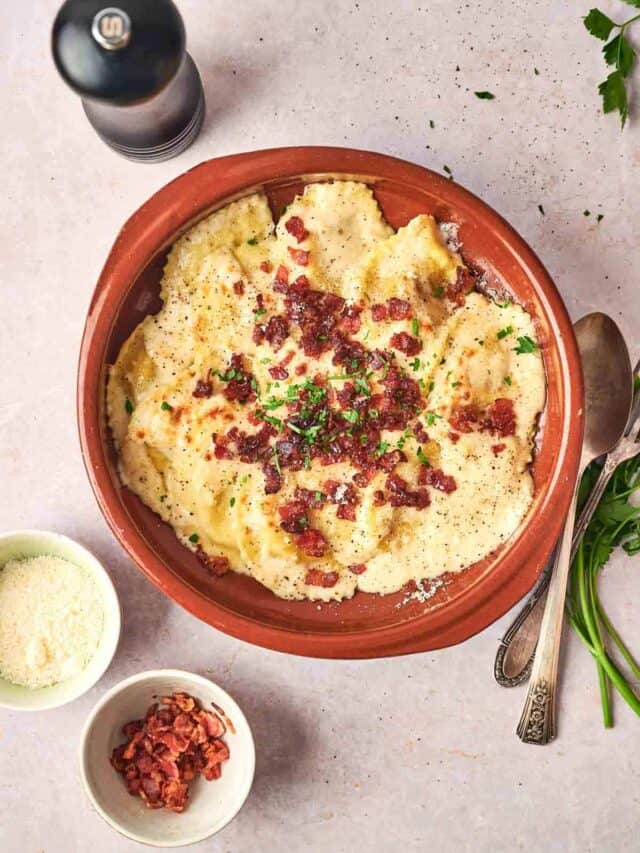Creamy mashed potatoes topped with bacon bits and fresh herbs, served in a rustic brown bowl with a spoon on the side, a pepper mill, and small bowls of additional toppings.