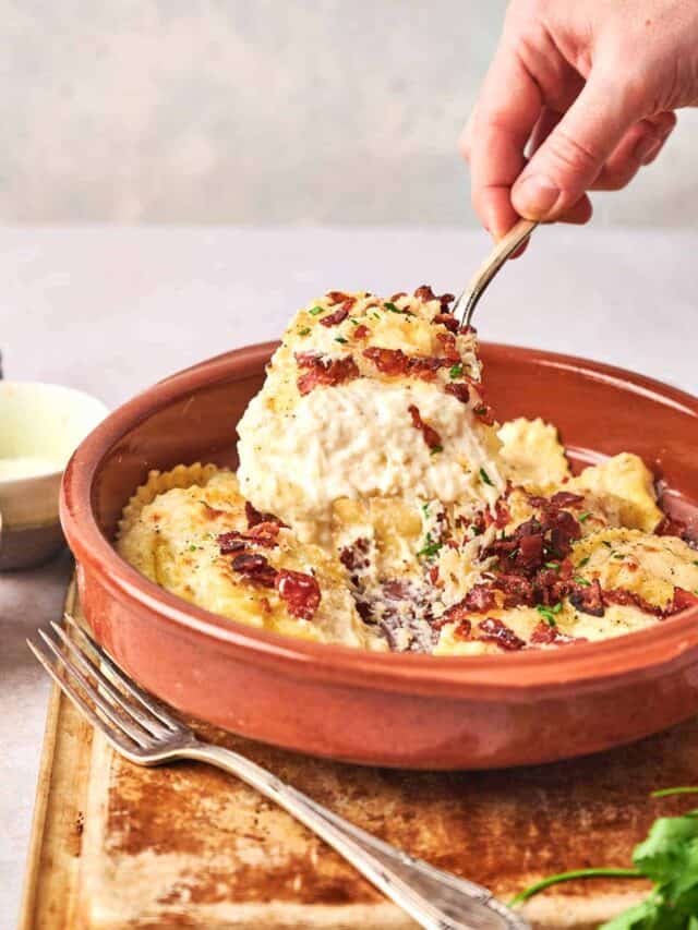 A person holding a fork over a bowl of Olive Garden's Ravioli Carbonara.