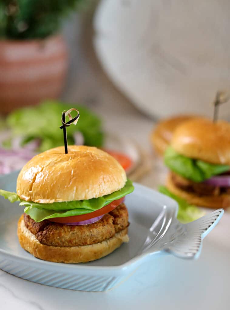 Two air fryer tuna sandwiches on a plate with lettuce, tomato, and red onion, garnished with a toothpick.