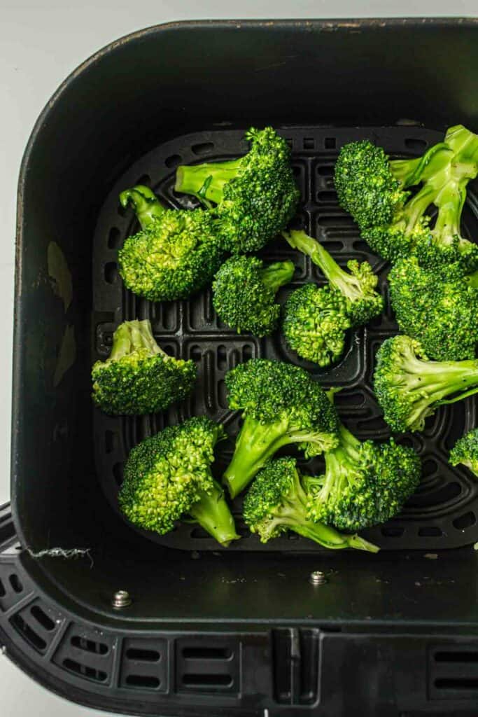 Fresh broccoli florets arranged in an air fryer basket, ready to be cooked.