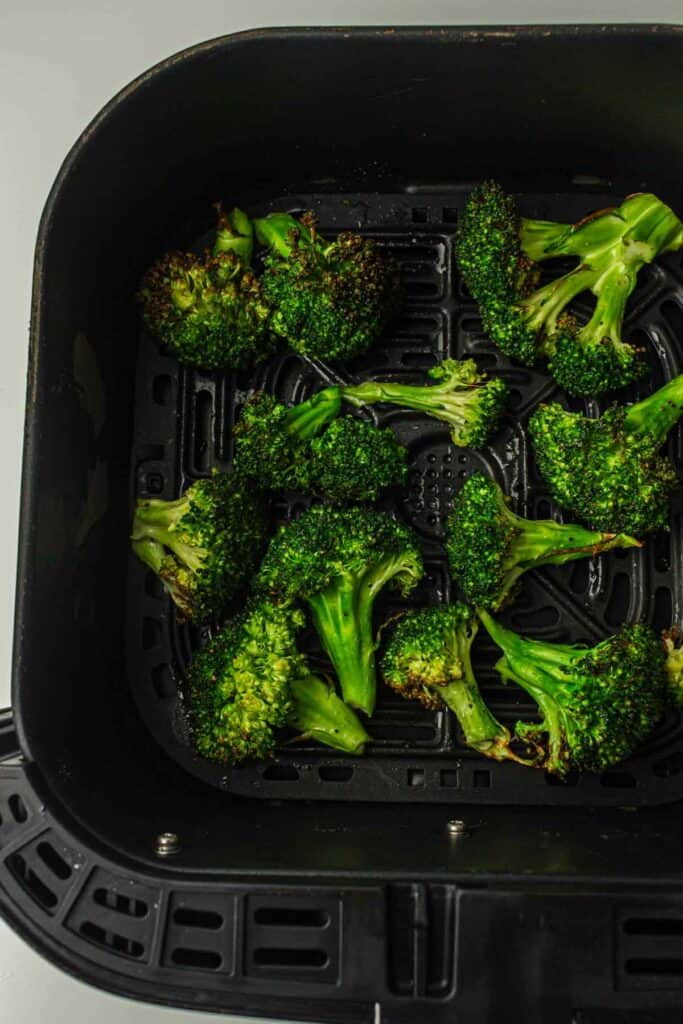 Roasted broccoli florets in an air fryer basket.