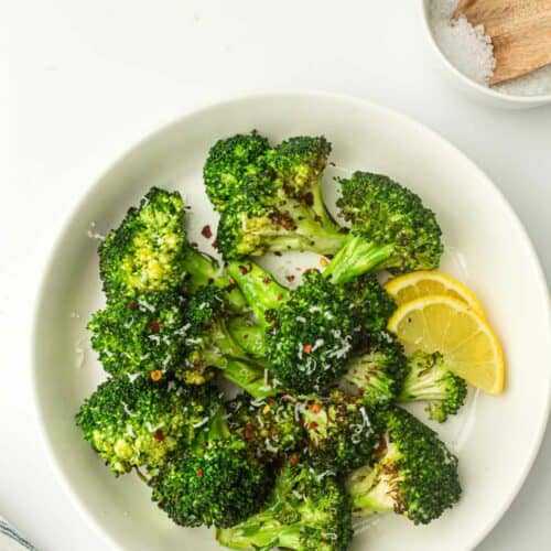 A plate of roasted broccoli seasoned with spices and garnished with lemon slices.