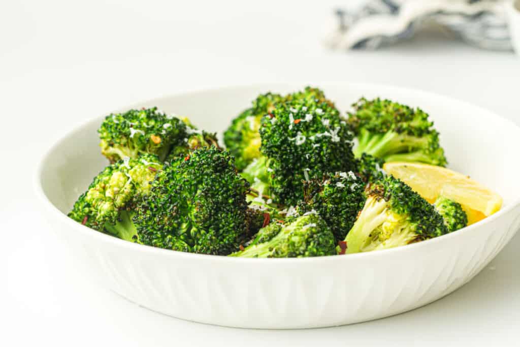A bowl of air-fried broccoli seasoned with spices and garnished with lemon wedges.