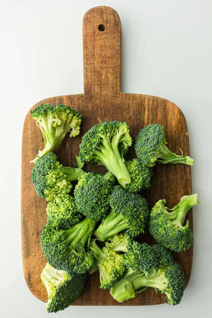 Fresh broccoli florets arranged on a wooden cutting board.