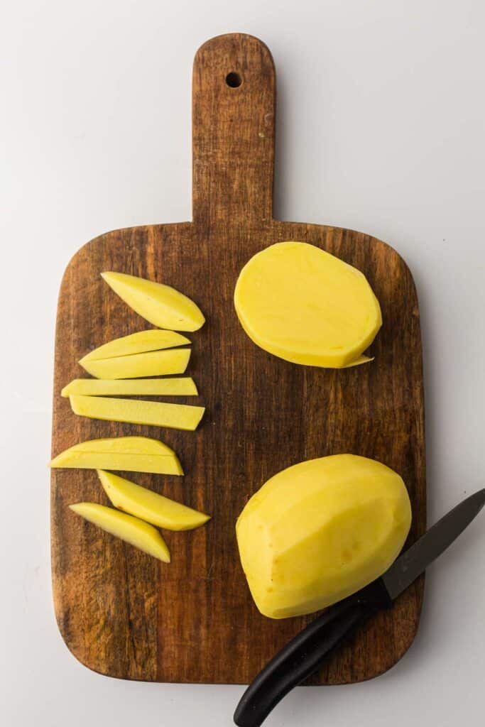 Sliced potatoes on a wooden cutting board with a knife.