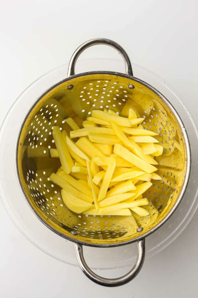 Sliced potatoes in a metal colander.
