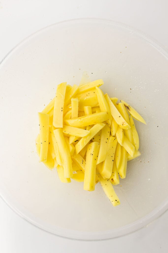 Sliced raw potatoes seasoned with spices in a clear bowl.