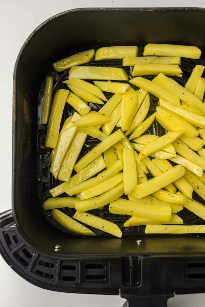 Sliced potatoes seasoned and ready for cooking in an air fryer basket.