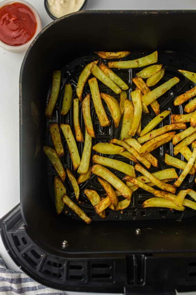 Seasoned potato slices in an air fryer basket.