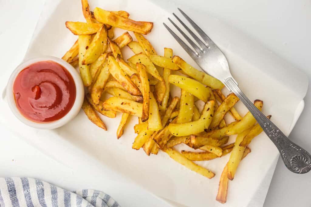 A plate of seasoned air-fried fries with a side of ketchup and a fork.