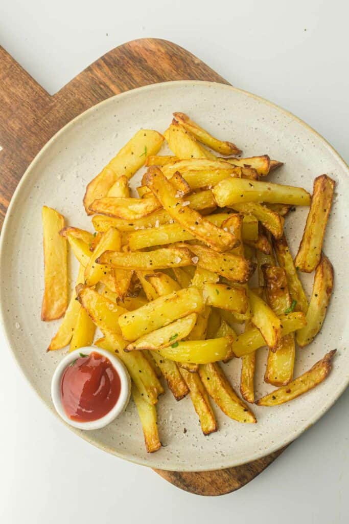 A plate of golden-brown air-fried French fries served with a side of ketchup.