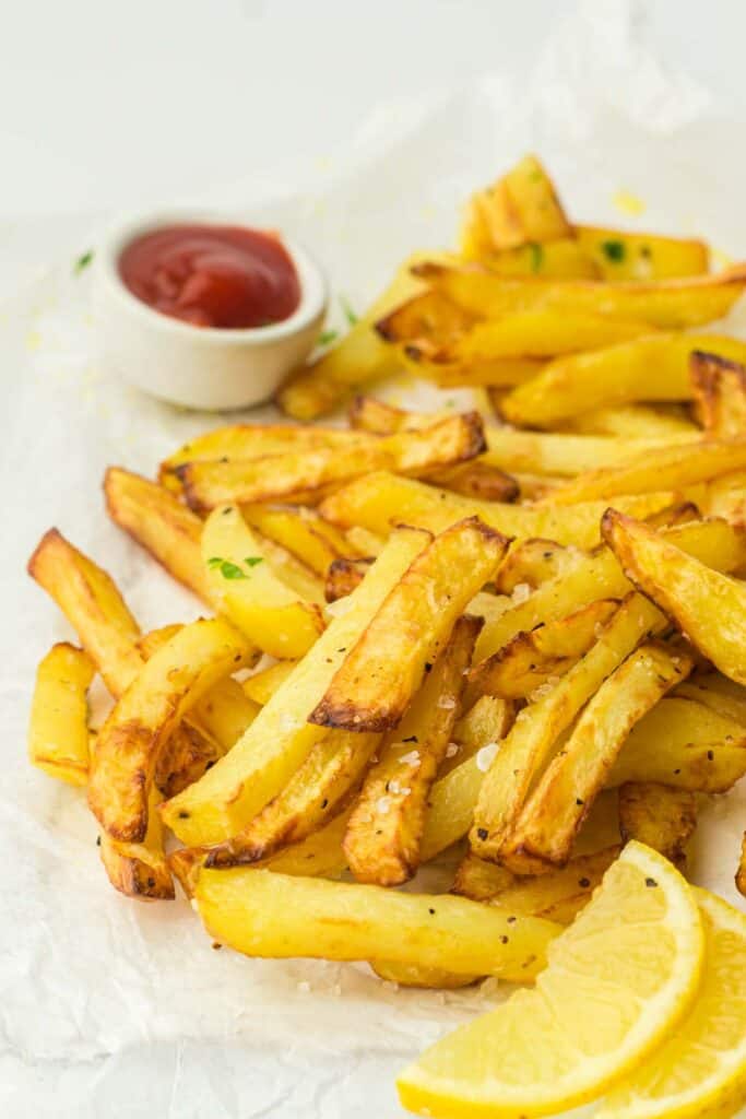 A serving of golden-brown air-fried French fries with a side of ketchup and lemon wedges.
