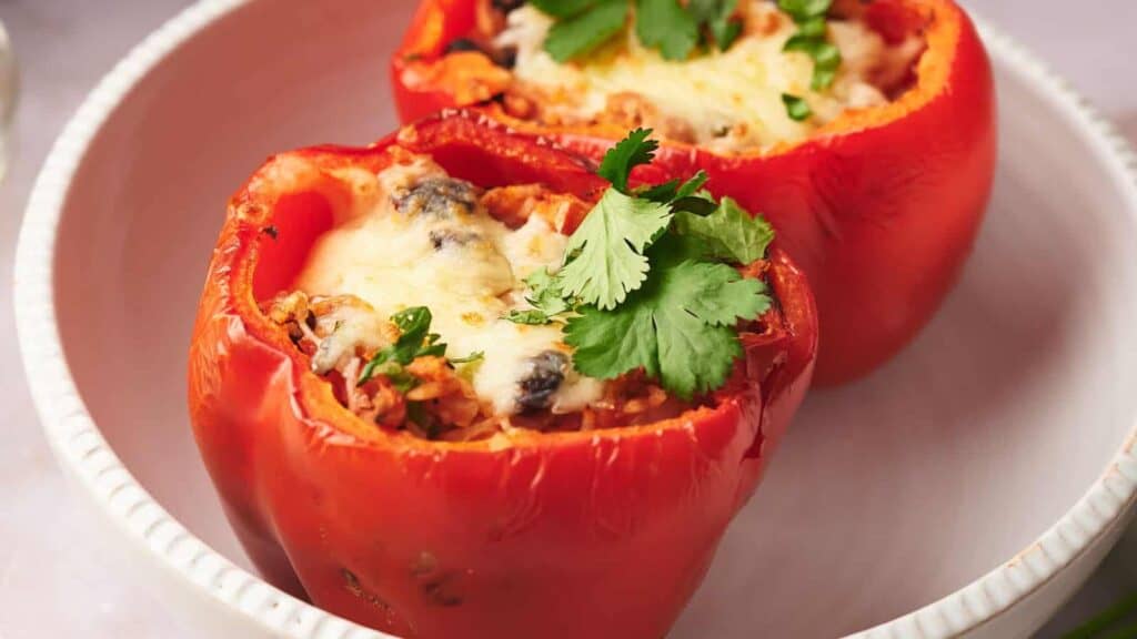 Stuffed bell peppers topped with melted cheese and garnished with a cilantro leaf.