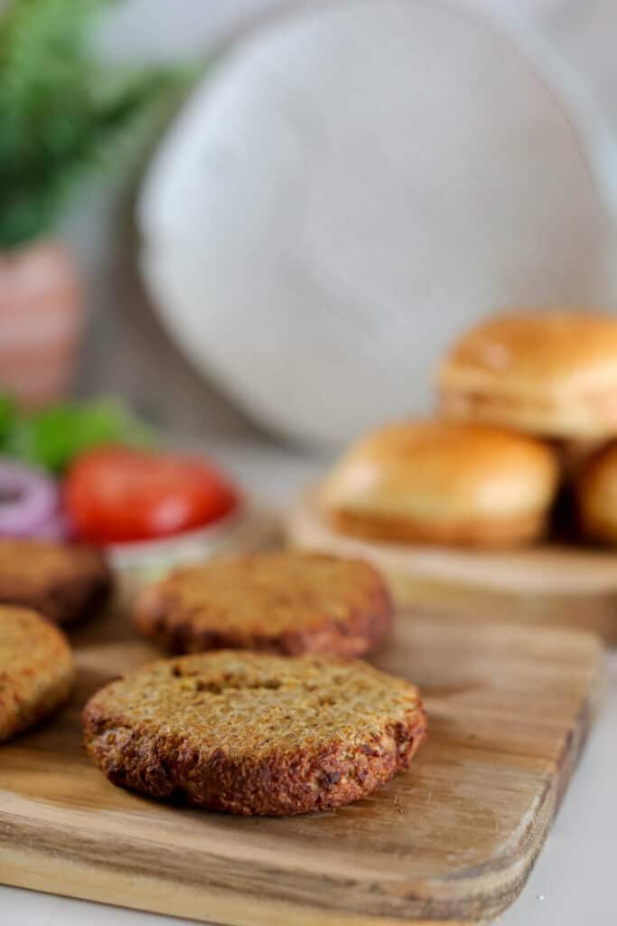 Homemade veggie burgers on a wooden cutting board with air fryer buns and fresh vegetables in the background.
