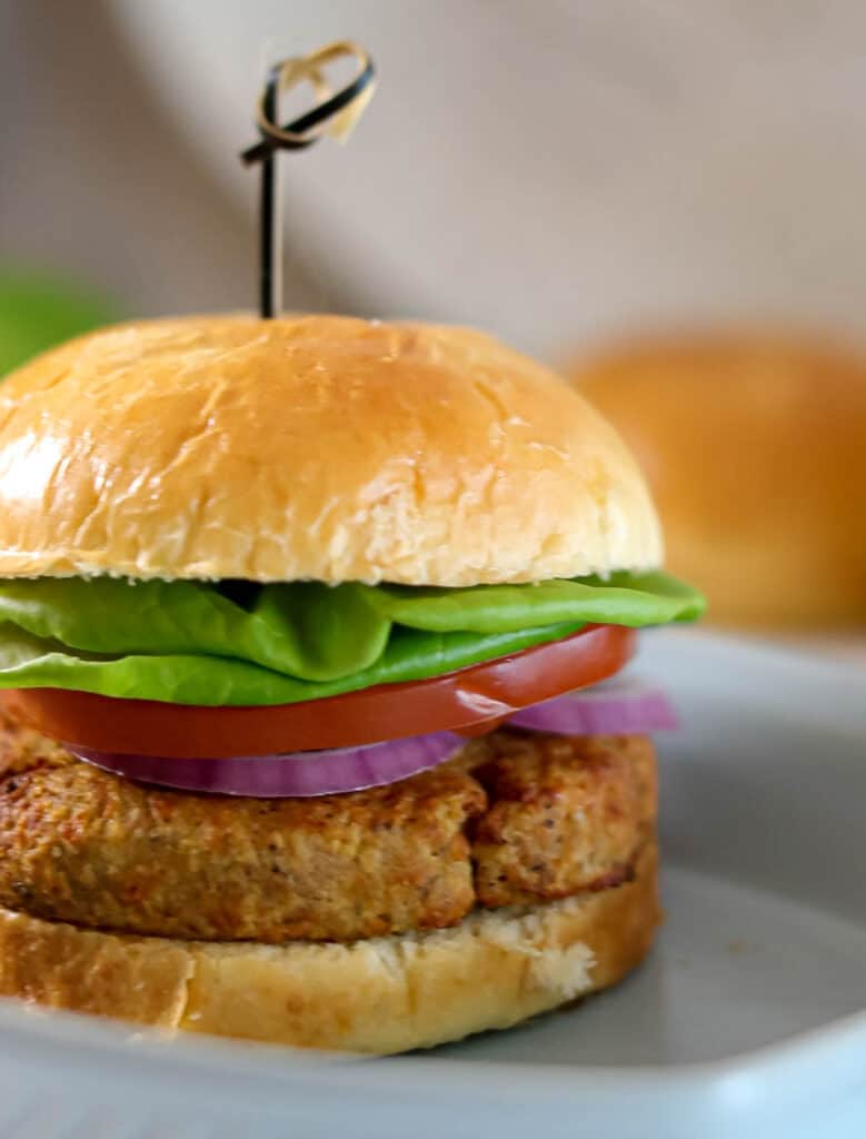An air fryer tuna sandwich with lettuce and tomato on a white plate in an air fryer.