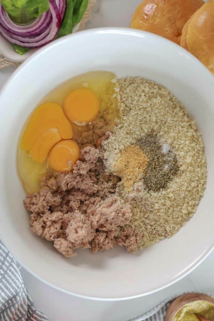 Ingredients for a recipe, including eggs, ground tuna, breadcrumbs, and spices in a bowl.