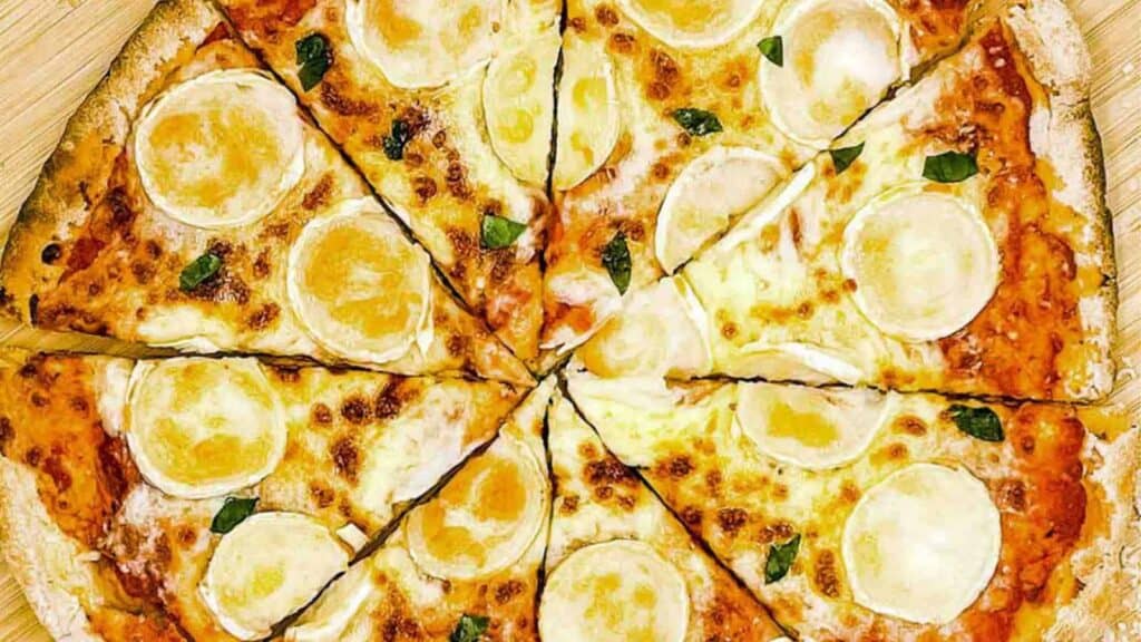 A pizza with cheese cut in half on a wooden board.