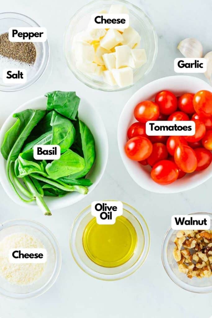 Various fresh ingredients labeled for preparing Caprese Pesto Tarts, including cheese, garlic, tomatoes, basil, olive oil, walnuts, salt, and pepper.