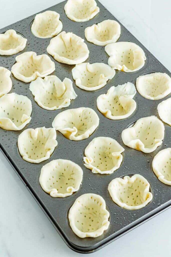 Unbaked pastry shells arranged in a muffin tin, ready to be filled with Caprese Pesto Tarts or baked.