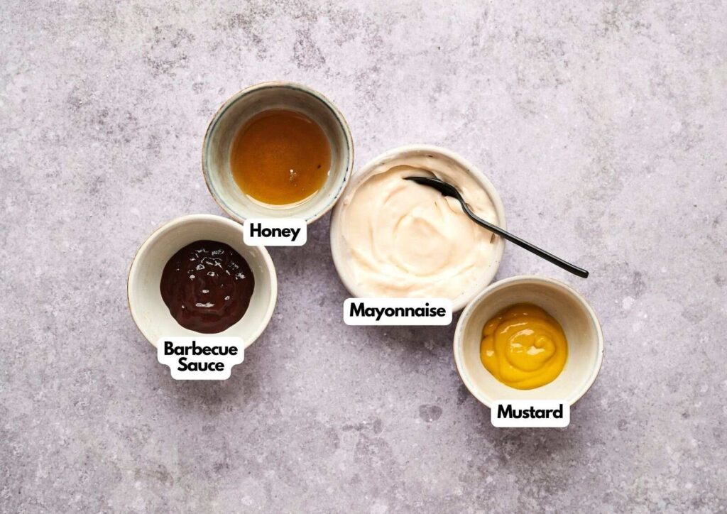 Four small bowls containing ingredients for homemade Chick-fil-A sauce: honey, mayonnaise with a spoon, barbecue sauce, and mustard, arranged on a light countertop.