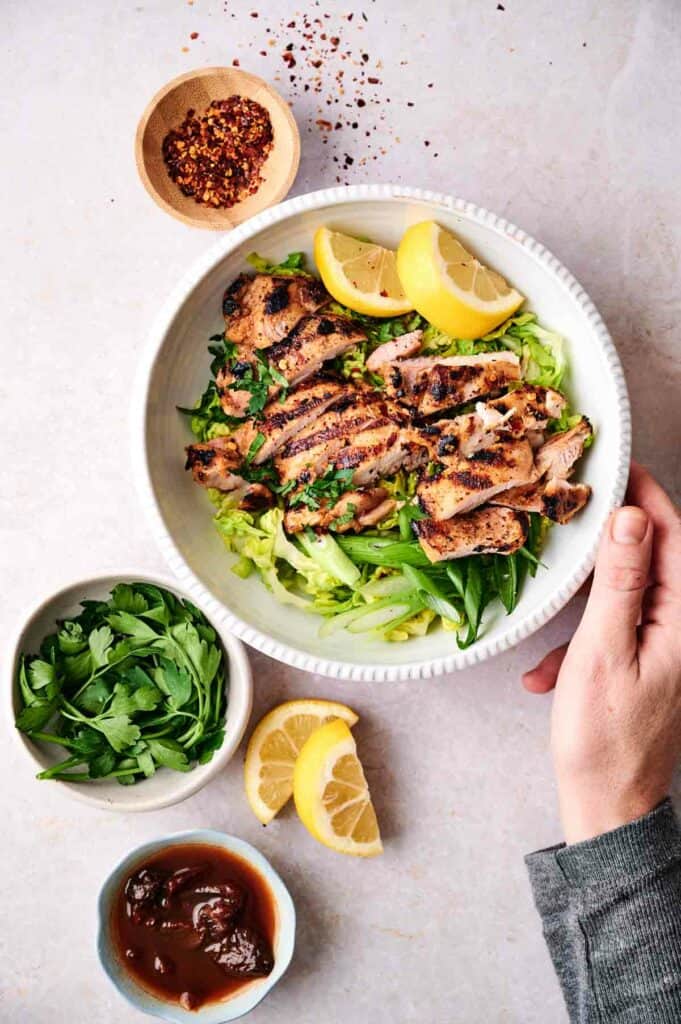 Chipotle Grilled Chicken with slices of lemon in a bowl and other ingredients on the side.