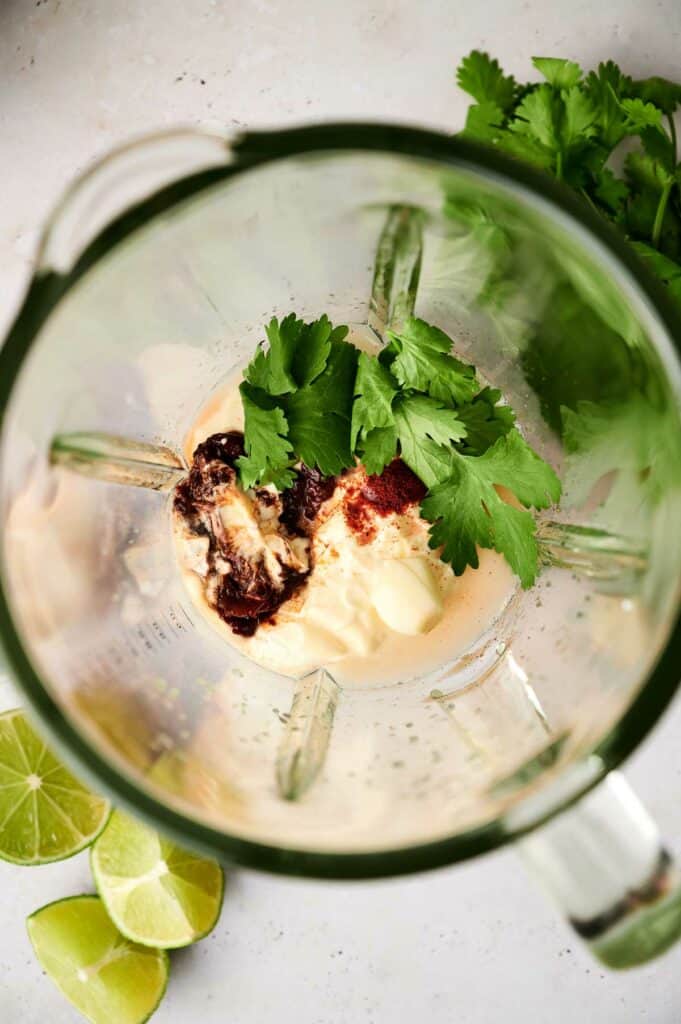 Ingredients for a chipotle sauce in a blender, including herbs, spices, and citrus.