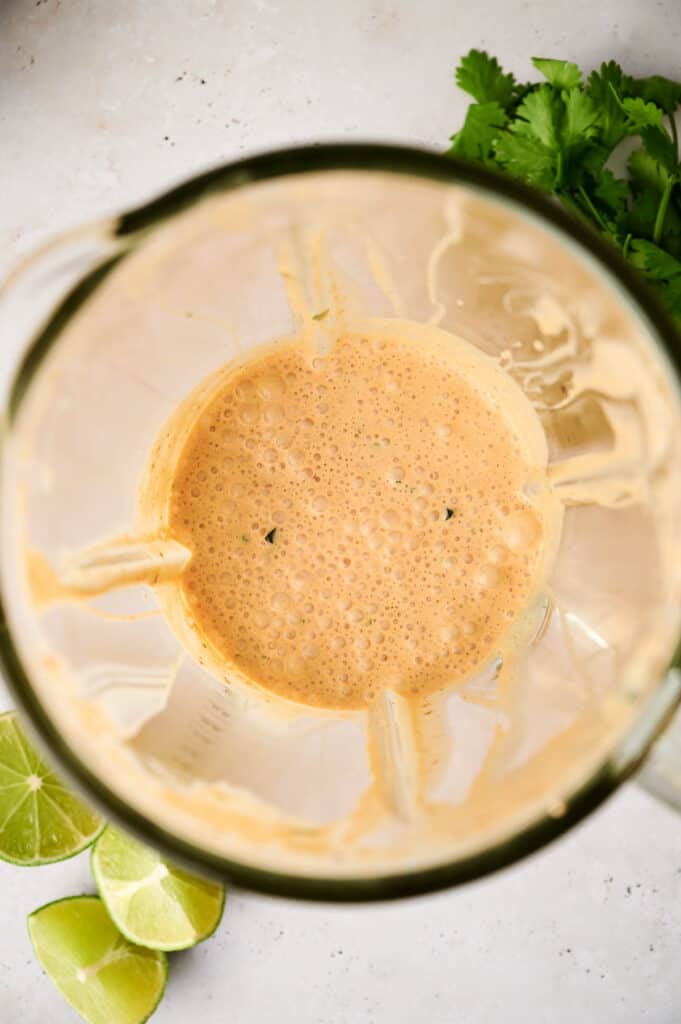 Top view of freshly blended chipotle sauce with herbs and lime wedges on the side.