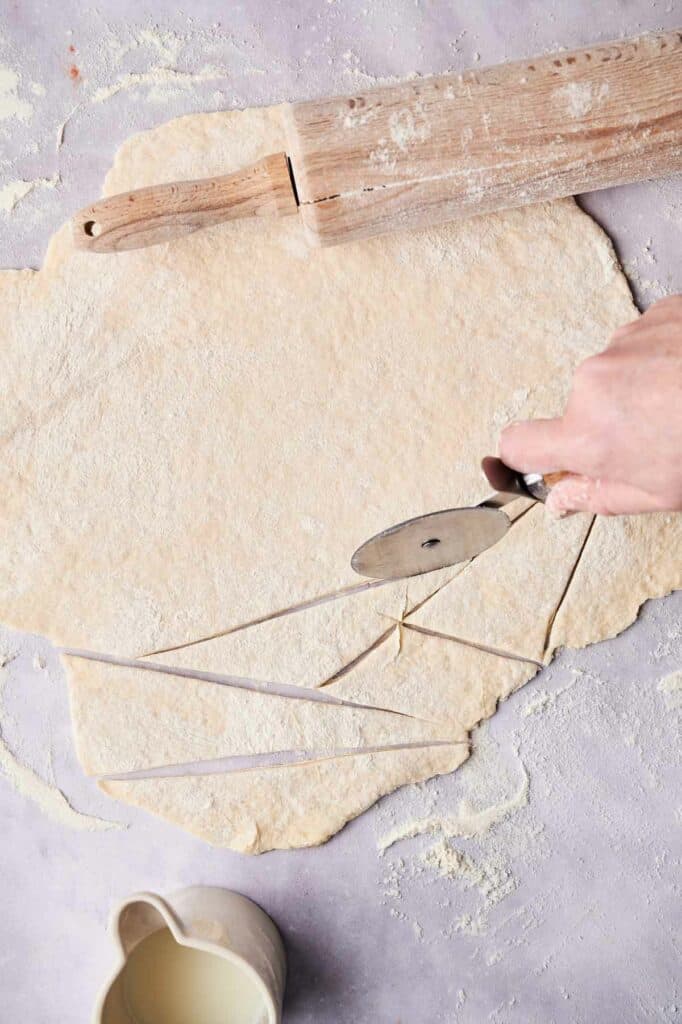 Rolling out dough and cutting it with a pastry cutter on a floured surface for Cracker Barrel Chicken and Dumplings.