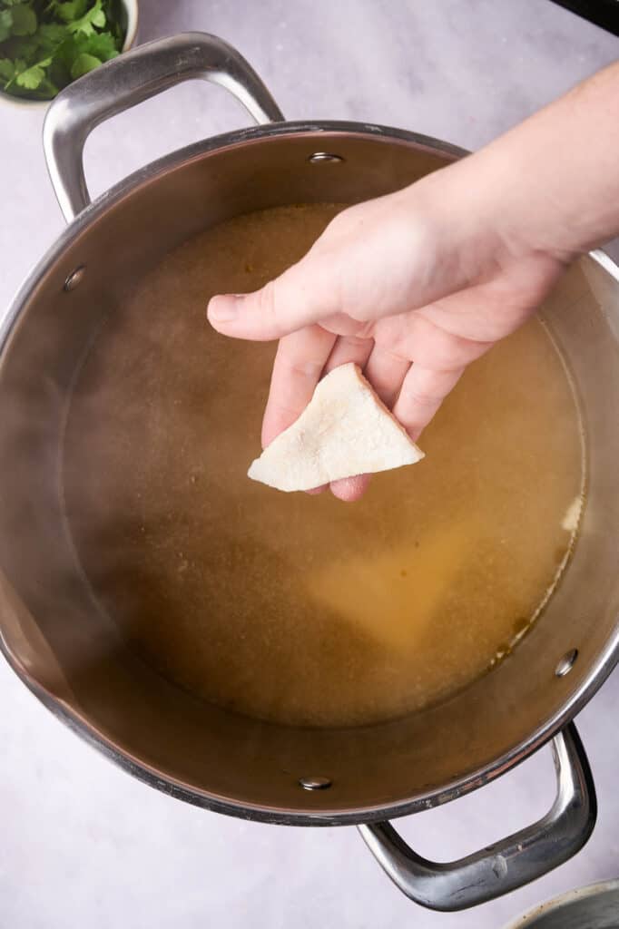 A hand adding dumplings into a pot for a cracker barrel chicken soup.