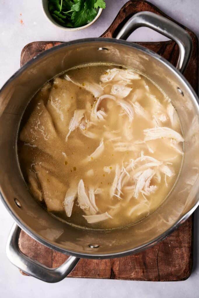 Chicken and Dumplings soup in a stainless steel pot on a wooden board, viewed from above.